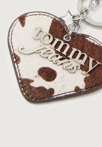 Hjerteformet nøkkelring med brun og hvit kuhårmønster og sølvtekst "tommy jeans" samt stjernesjarm på en metallring.