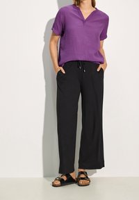 Top viola a maniche corte con scollatura a V, abbinato a pantaloni neri a gamba larga con coulisse. Indossato con sandali neri.