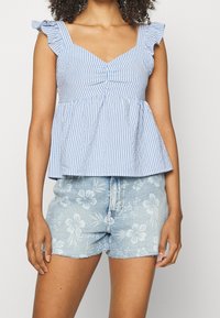 Haut péplum rayé bleu et blanc avec bretelles à volants, présentant un devant froncé. Associé à un short en denim bleu clair à motif floral.