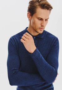 Granatowa, długi rękaw polo z miękkiej tkaniny, z kołnierzykiem na dwa guziki, dopasowanym kroju i ściągaczami na rękawach; gładkie wykończenie materiału.