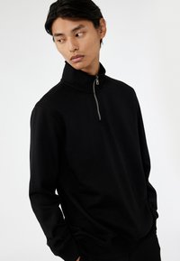 Zwarte zip-up sweatshirt met hoge kraag, lange mouwen en zacht materiaal met een gladde textuur en minimalistisch ontwerp.