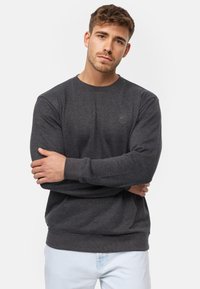 Sudadera de color gris oscuro hecha de tela suave, con un escote redondo, puños acanalados y un pequeño detalle de logo en el pecho.