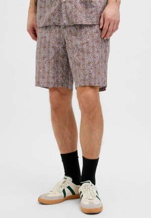 Brown patterned shorts with geometric design, made from lightweight fabric. Paired with white sneakers featuring green stripes and black socks.