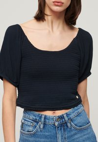 Mørkeblå, kortærmet cropped top med tekstureret stof, firkantet halsudskæring og subtile rynkedetaljer, parret med højtaljede denim jeans.
