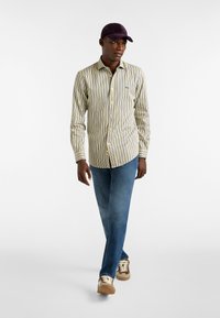 Napapiri yläpaitaan sinisistä ja keltaisista pystysuorista raidoista, slim fit, yhdistetty sinisiin farkkuihin ja vaaleisiin tennareihin, korostettuna tummalla lippalakilla.