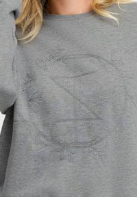 Sudadera gris con un diseño circular texturizado, adornado con acentos florales y un logotipo estilizado, hecha de una tela suave y ligera.