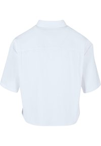 Chemise blanche unie à manches courtes avec un ourlet droit et un col montant, vue de dos sur un fond blanc.