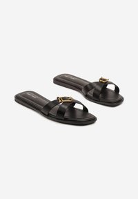 Sandales plates noires avec des brides mates croisées et une boucle dorée en accent. La semelle est plate et lisse, avec un design minimaliste.