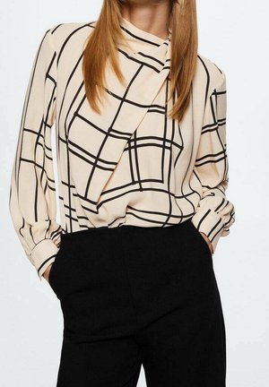 Blouse crème à motif quadrillé noir, manches longues, avec un détail torsadé au niveau de l'encolure ; associée à un pantalon noir taille haute.