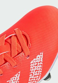 Punttikengän muotoilu, jossa on tekstuuri, näkyvä valkoinen logo ja nauhat. Ylätasku on sileä, vahvistetuilla nauha-aukkoilla ja nappuloilla.