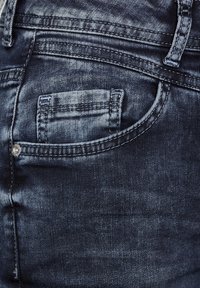 Jeans in denim blu scuro con una piccola tasca frontale, cuciture in evidenza e una texture consumata, evidenziando un aspetto logoro.