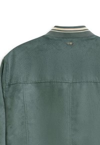 Grüne, perforierte Jacke mit einem gestreiften Kragen, die eine Naht am Rücken und ein kleines Markenschild nahe dem Halsausschnitt aufweist.