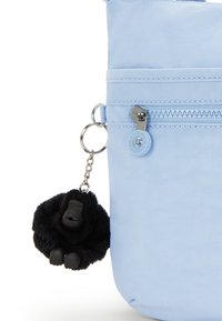 Bustina blu chiaro con finitura in nylon testurizzato, dotata di tasca con zip e un portachiavi a forma di gorilla nera come dettaglio. Il tirazip è metallico.