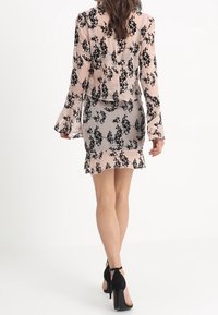 Ljusrosa blommig blus med svarta mönster, tillsammans med en figurnära, genomskinlig svart kjol. Svarta högklackade skor fulländar outfiten.