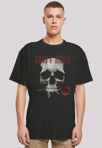 Camiseta de algodón negra con un gráfico de una calavera sosteniendo una rosa roja, con el texto "GUNS N' ROSES" arriba en rojo negrita.