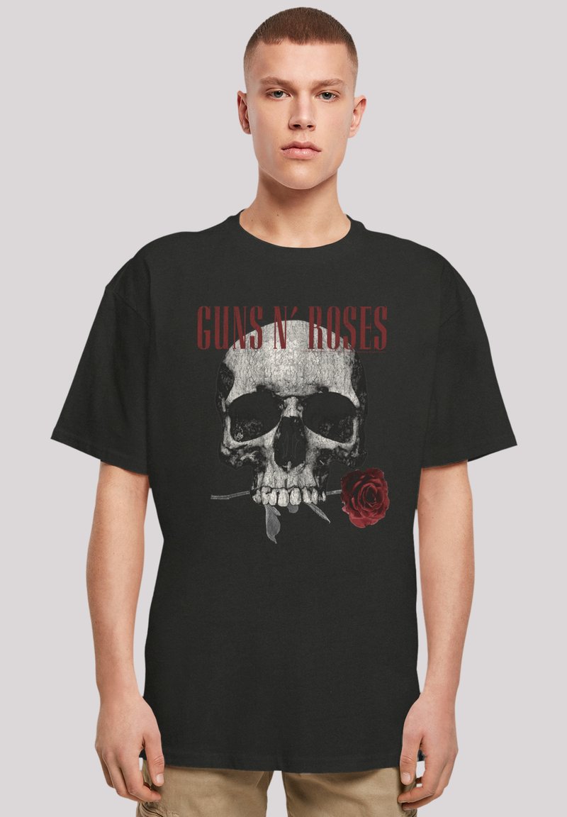 Camiseta de algodón negra con un gráfico de una calavera sosteniendo una rosa roja, con el texto "GUNS N' ROSES" arriba en rojo negrita.