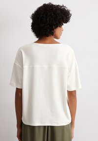 White, loose-fitting t-shirt with short sleeves, featuring a wide neckline and a clean, minimal design without visible logos or patterns.