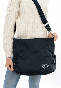 Borsa a spalla nera in tessuto con superficie testurizzata, tracolla regolabile, accessori in metallo e logo stampato sulla parte anteriore.