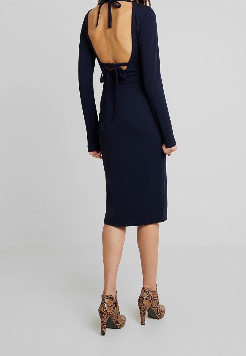 Tummansininen, pitkähihaiset mekko, jossa on syvä selkäleikkaus ja solmimisyksityiskohta kaulassa. Yhdistetty käärmekuvioisiin korkeakorkoisiin saappaisiin.