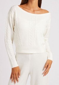 Weißer, geknoteter, verkürzter Pullover mit weitem Halsausschnitt und langen Ärmeln. Weiche Textur mit erhabenen Mustern entlang der Vorderseite und Ärmeln.