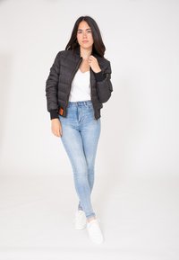 Czarna kurtka puchowa o skróconym kroju, z prążkowanymi mankietami i zamkiem z przodu. Połączona z jasnoniebieskimi spodniami typu high-waisted i białymi trampkami.