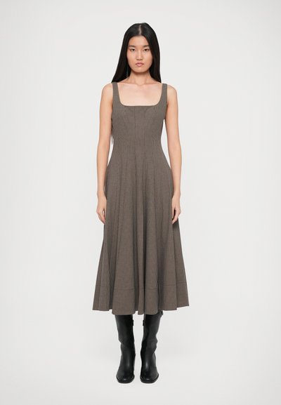 Robe midi à carreaux marron avec un décolleté carré et des bretelles larges, dotée d'un corsage ajusté qui s'épanouit en une jupe fluide. Associée à des bottes noires.