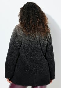 Musta ja harmaa ombre-tekstuurinen fleece-takki, jossa on rento malli, leveät hihat ja pyöreä helma, nähtynä takaa.