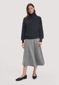 Dunkler Rollkragenpullover mit langen Ärmeln, kombiniert mit einem knielangen, hellgrauen Schwingrock. Das Ensemble zeichnet sich durch glatte Texturen und eine schlichte Silhouette aus.