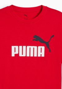 Punainen puuvillapaita, jossa on musta hyppivä pumalogo ja rohkea valkoinen "PUMA" -teksti. Klassinen pyöreä pääntie ja lyhythihaiset hihat.
