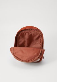 Oranssi pehmolelureppu, jossa on pehmeä rakenne ja vetoketju. Sisäpuoli on vuorattu sileällä satiinikankaalla, joka on samaa väriä.