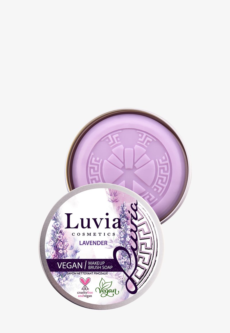 Luvia laventeli vegaaninen meikkisiveltimen saippua pyöreässä tinassa. Vaaleanlila saippua, jossa on kuvioitu pinta, ja joka on varustettu kukkakuviolla ja logoilla.