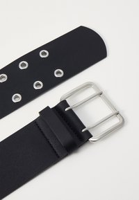 Schwarzer Leder-Gürtel mit silberner Metallschnalle, ausgestattet mit mehreren kreisförmigen Ösen und einer glatten Textur, entworfen für eine verstellbare Größe.