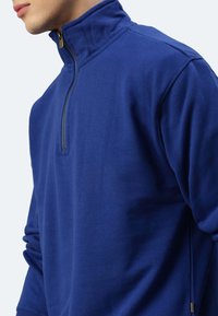 Marineblaues, mit Reißverschluss versehenes Fleece mit hohem Kragen, ausgestattet mit einem seitlichen Reißverschluss und strukturierter Oberfläche. Bequeme Passform, seitlich gezeigt.