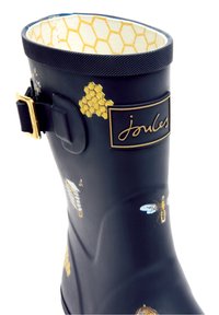Botte de pluie bleu marine avec un motif en nid d'abeille à l'intérieur, des graphismes de abeilles et de rayons de miel à l'extérieur, et une boucle dorée sur le côté.