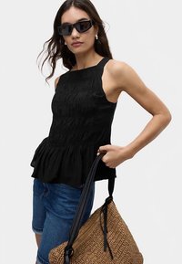 Czarny top bez rękawów z teksturowanym marszczeniem, falbaną na dole i zaokrąglonym dekoltem. W zestawie ze szortami dżinsowymi i plecioną torebką.