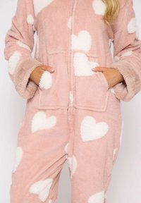 Rosenfarvet, fluffy jumpsuit med hvide hjerte-mønstre, der har lynlås foran, to forlommer og brede manchetter. Blød tekstur og hyggelig pasform.