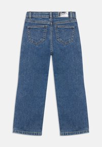 Jeans largos de ganga azuis com uma cintura média, apresentando dois bolsos traseiros e uma bainha desfiada. A costura é visível ao longo das costuras.
