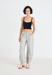 Zwarte cropped tanktop, losvallende grijze broek met slangenpatroon, en roze sneakers met donkere accenten; een gladde textuur en een casual ontwerp.