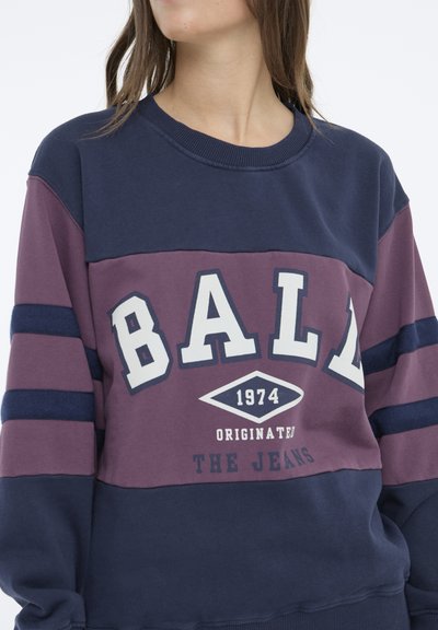 Hanorac bleumarin și vin cu text alb „BALL”, anul „1974”, și dungi. Material moale cu guler rotund și manșete ribbate.