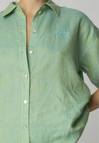Camicia a maniche corte con bottoni in misto lino verde chiaro, caratterizzata da un sottile motivo testurizzato e un logo ricamato blu sul petto.