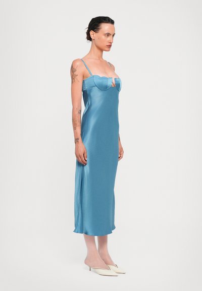 Soupav satin midi kleit helesinisest tooni, millel on õhukesed nööbid ja laineline kaelus. Sile tekstuur ja kehakujuline lõige, koos kreemjate kontsadega.