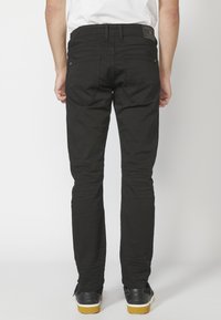 Fekete slim-fit farmernadrág öt zsebbel, kontrasztos varrással és bőr címkével a derékrészen. Simább textúra, egyenes szabás.