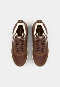 Brown high-top sneakers featuring a mix of smooth and textured materials, white lining, and contrasting laces in brown and white patterns.