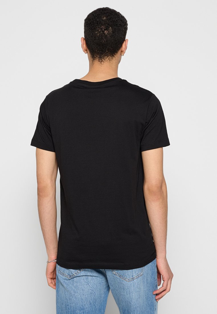 T-shirt en coton noir avec un col rond classique. Manches courtes et ourlet droit, porté avec un jean bleu clair.