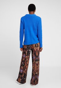 Blauwe, gestructureerde gebreide trui met een ronde halslijn en lange mouwen, gecombineerd met zwarte wijde broek met een kleurrijk paisleypatroon.