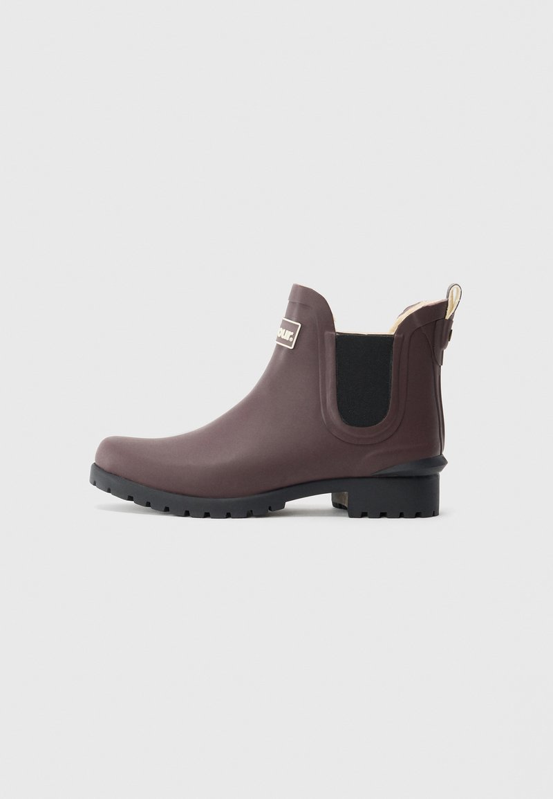 Bota de chuva castanha até ao tornozelo com painéis laterais elásticos pretos e sola de tração preta, vista do lado exterior sobre um fundo claro e liso.