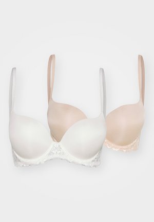 Twee bh's: een witte met kantafwerking en voorgevormde cups, een beige met gladde cups. Beide hebben verstelbare bandjes en een naadloos ontwerp.