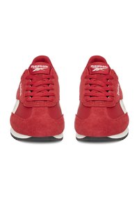 Punased sametist jooksujalad valgete detailidega, klassikalise lipsuga disainiga ja ümarate varvastega. Must kummist tald, minimaalne bränding.