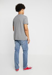 Camiseta gris de manga corta con un corte regular, combinada con jeans de mezclilla azul y zapatillas rojas. El fondo es completamente blanco.