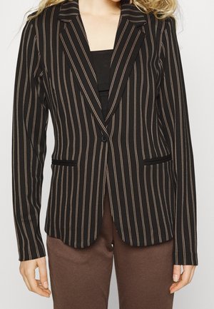 Blazer negro con finas rayas blancas verticales, cierre de un solo botón, usado sobre una camiseta negra, combinado con pantalones marrones.